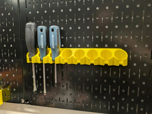 A yellow wall-mounted screwdriver organizer rack holding three screwdrivers with black and gray handles, attached to a black metal Wall Control pegboard.